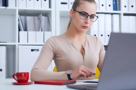Young beauiful Caucasian businesswoman in glasses working on notebook computer and business document at office.の写真素材