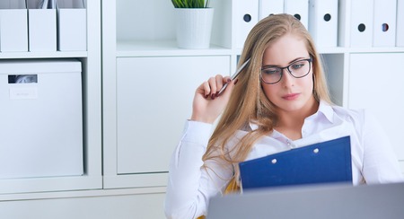 Young beauiful Caucasian businesswoman in glasses intently working on notebook computer and business document at office.の写真素材