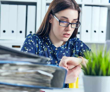 Shocked female manager looking at her watch near a pile of documents. Deadline concept.の写真素材