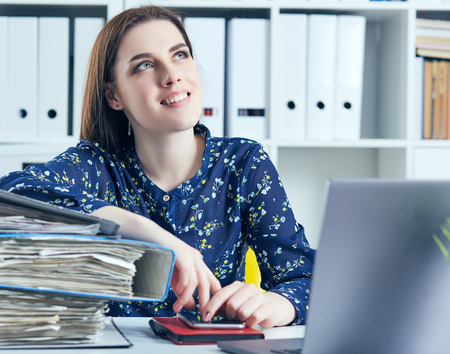 Business woman or secretary with many documents folders bills on her desk taking break, relaxing at work thinking day dreaming.の写真素材