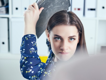 Angry business woman with folder trying to hit his colleague in office. Stressful situations at work.の写真素材