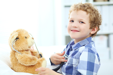 Little curly Caucasian boy plays in doctor with stethoscope and Teddy Bear.の写真素材