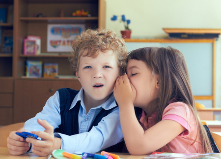 Girl telling secret to surprised curly boy in classroom.の写真素材