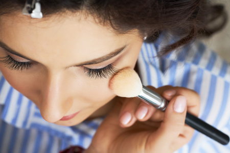 Master inflicts brush powder on the face of the girl, completes the day make-up in a beauty salon. Stylist at this time does a hairdo.の写真素材