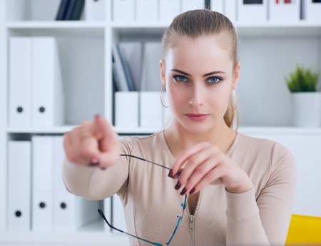 Angry Caucasian business woman sitting at her desk and pointing with finger to get outの写真素材