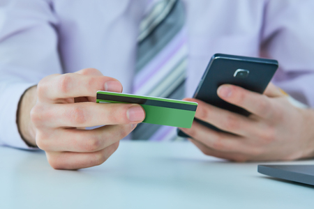 Mans hands holding a credit card and using smart phone for online shopping. Online paymentの写真素材