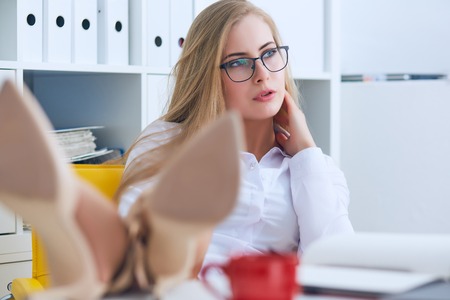 Young Caucasian business woman is relaxing at work holding hands behind head.の写真素材