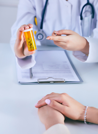 Female medicine doctor hand hold jar of pills and explain how to take pills to patient at worktable. Panacea and life save prescribing treatment legal drug store concept.の写真素材