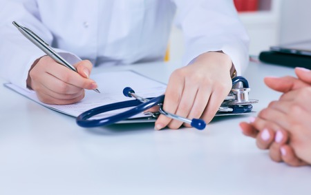 Close up of a female doctor filling up an application form while consulting patient. Medicine and health care conceptの写真素材