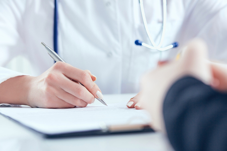 Doctor filling medical form while patient consultation. Patient sitting at doctor office. Diagnostic and prevention of women diseases, healthcare and medical service conceptの写真素材