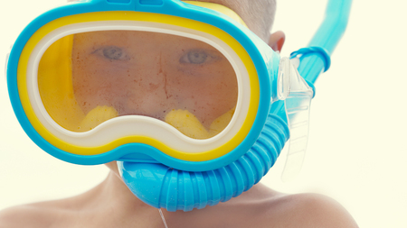 Little Caucasian boy playing with snorkeling equipment standing on sand on tropical beach.の写真素材
