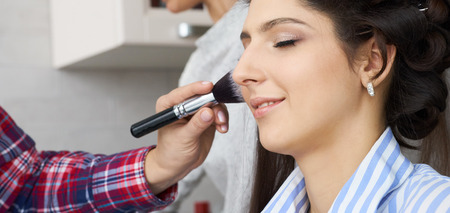 Master inflicts brush powder on the face of the girl, completes the day make-up in a beauty salon.の写真素材