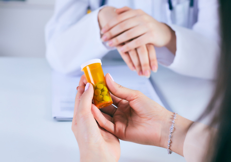 Female medicine doctor hand hold jar of pills and explain how to take pills to patient at worktable. Panacea and life save prescribing treatment legal drug store concept.の写真素材