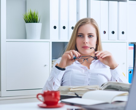 Confident business lady. Beautiful young woman in formalwear holding a paper and adjusting glasses while sitting at the office and loocing at the camera.の写真素材
