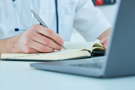 Male doctor or medical student holding ballpoint pen and writing on notepad. Therapist fills the patient admission scheduleの写真素材