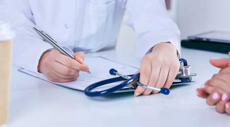 Close up of a female doctor filling up an application form while consulting patient. Medicine and health care conceptの写真素材