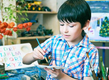 Young boy sitting in front of easel painting a fish, holding a brush in hand. Boy is getting ready to become an artist.の写真素材