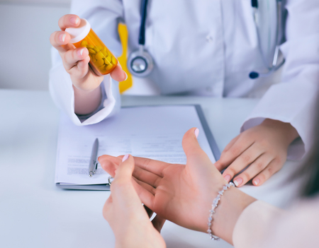 Female medicine doctor hand hold jar of pills and explain how to take pills to patient at worktable. Panacea and life save prescribing treatment legal drug store concept.の写真素材
