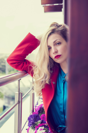 Outdoor fashion portrait of glamour young cheerful stylish lady wearing trendy red coat. Blonde long hair. Full lips, green eyes.の写真素材