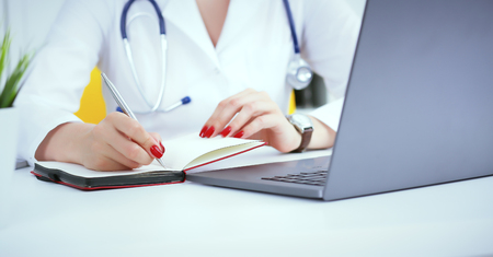 Female medicine doctor hand holding silver pen writing something on clipboard and working laptop closeup. Physician ready to examine patient and helpの写真素材