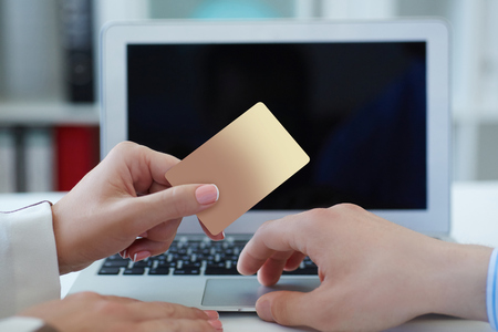 Woman showing a payment credit card with laptop at the background closeup . Business, freelance concept. Shallow depth of field with focus on the credit card.の写真素材