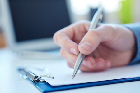 Male hand holding silver pen ready to make note in a clipboard. Businessman or employee at workplace writing business ideas, plans or tasks.の写真素材
