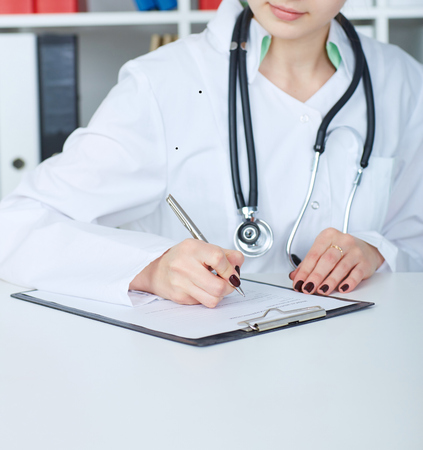 Close-up view of female doctor hands filling patient registration form.の写真素材