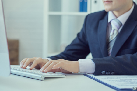 Male hands typing on desktop computer keyboard in office closeup.の写真素材