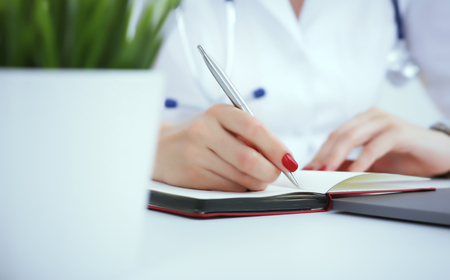 Female medicine doctor hand holding silver pen writing something on clipboard and working laptop closeup. Physician ready to examine patient and helpの写真素材