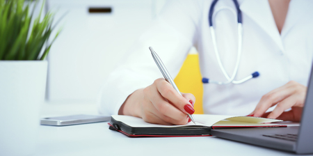 Female medicine doctor hand holding silver pen writing something on clipboard and working laptop closeup. Physician ready to examine patient and helpの写真素材