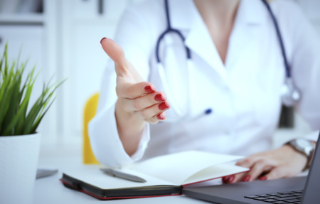 Female doctor making welcome gesture, inviting patient to sit down in medical office. Photo with depth of field.の写真素材