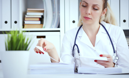 Bureaucracy in the hospital. Young female doctor work with stacks of files.の写真素材