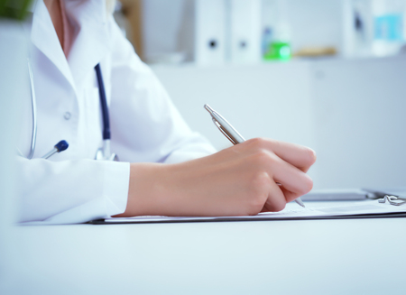 Front view of female doctor holding silver pen filling patient history list at clipboard pad. Physical exam or disease prevention.の写真素材