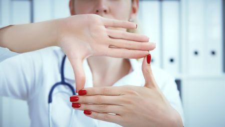 Young female doctor holding hands with advertising area between them and smiling on medical office in background. Photo with depth of fieldの写真素材