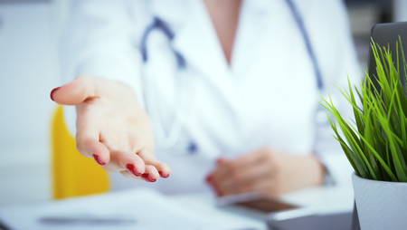 Female doctor making welcome gesture, politely inviting patient to sit down in medical office. Photo with depth of field.の写真素材