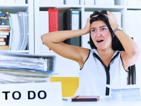 Young female office worker shocked by the huge amount of paper work. Deadline concepts.の写真素材