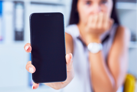 Young sad woman showing a blank smartphone screen. Focus on smartphone. Free space for your message.の写真素材