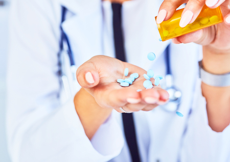 Pills are poured into female doctor hand from a jar, pills in hand, blue vitamins, orange jar with tablets, close-up.の写真素材