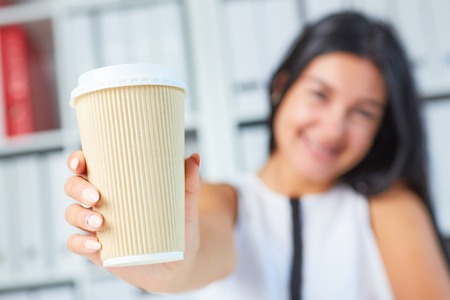 Girl showing paper cup of coffee in his hands close up. American paper eco cup. Girl drinking coffee indoors.の写真素材