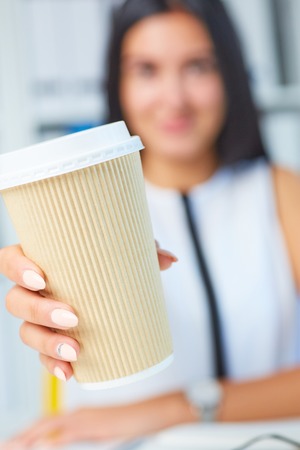 Girl showing paper cup of coffee in his hands close up. American paper eco cup. Girl drinking coffee indoors.の写真素材