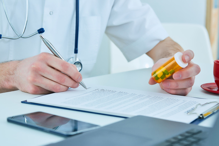 Close up of male doctors hand writing prescription paper and capsules.の写真素材