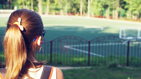 Young beautiful woman in sunny glasses at the stadium. The girl looks forward. View from the back.の写真素材