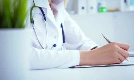Front view of female doctor holding silver pen filling patient history list at clipboard pad. Physical exam or disease prevention.の写真素材