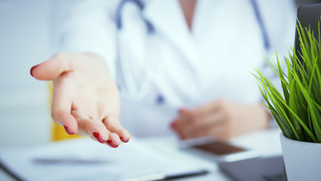 Female doctor making welcome gesture, politely inviting patient to sit down in medical office. Photo with depth of field.の写真素材