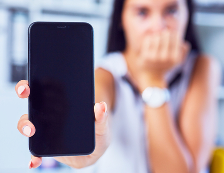 Young sad woman showing a blank smartphone screen. Focus on smartphone. Free space for your message.の写真素材