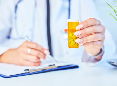 Female medicine doctor with jar of pills and write prescription to patient at worktable. Panacea and life save prescribing treatment legal drug store concept.の写真素材
