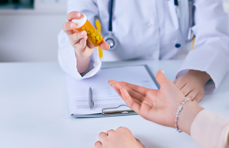 Female medicine doctor hand hold jar of pills and explain how to take pills to patient at worktable. Panacea and life save prescribing treatment legal drug store concept.の写真素材