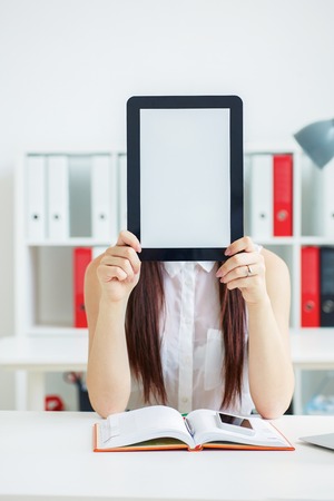 Female hands holding tablet in front of her face with copy space for text or picture. Stylish modern office workplace on a background.の写真素材