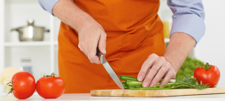 Mid section of a senior man with a knife cuting green onion on the kitchen background.の写真素材