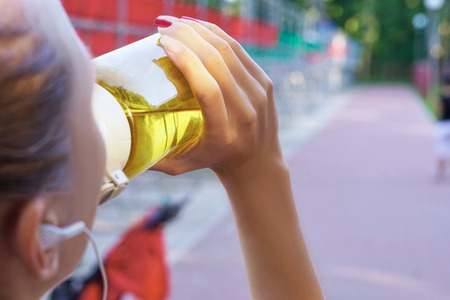 Young beautiful sportwoman drinking water at summer green park.の写真素材